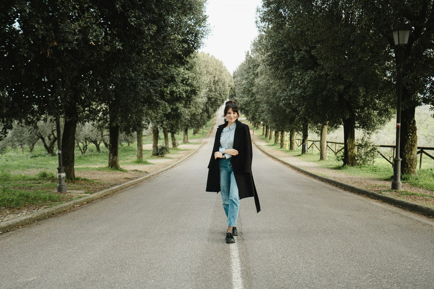 A woman walking alone along a quiet tree lined road