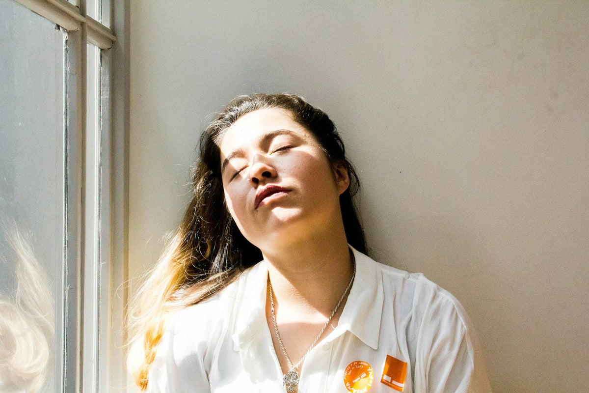 A woman sitting quietly by a window with her eyes closed in soft daylight