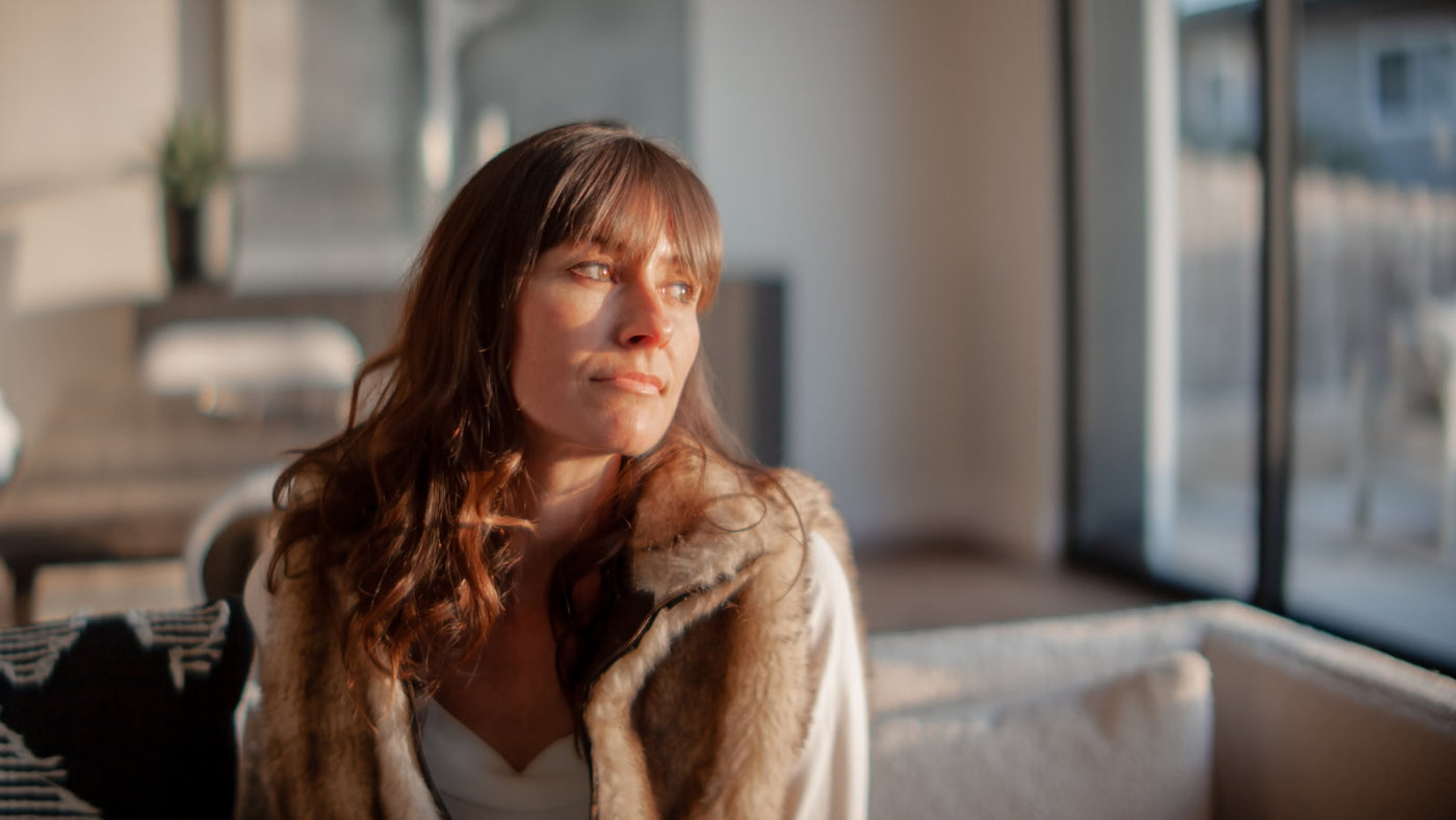 A woman sitting thoughtfully on a sofa in a warmly lit living room