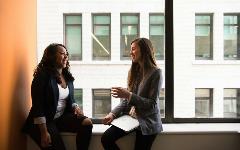 Two women sitting by a window in warm light, in the middle of a conversation