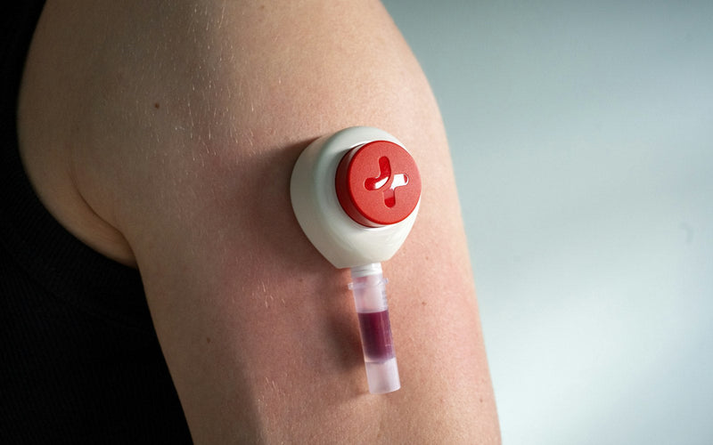 A small at-home blood collection device on the upper arm, filling a sample tube